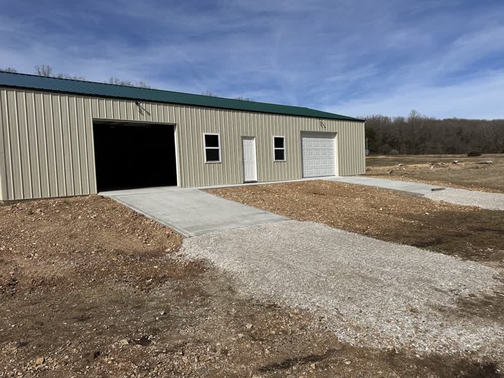 Finished concrete driveway apron leading up to a metal shop building, with graded gravel approach