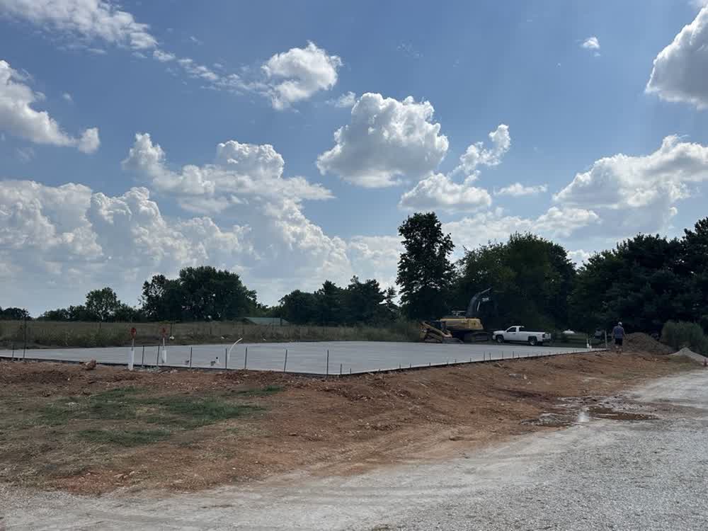 Large finished concrete pad on a graded building site with excavator on site